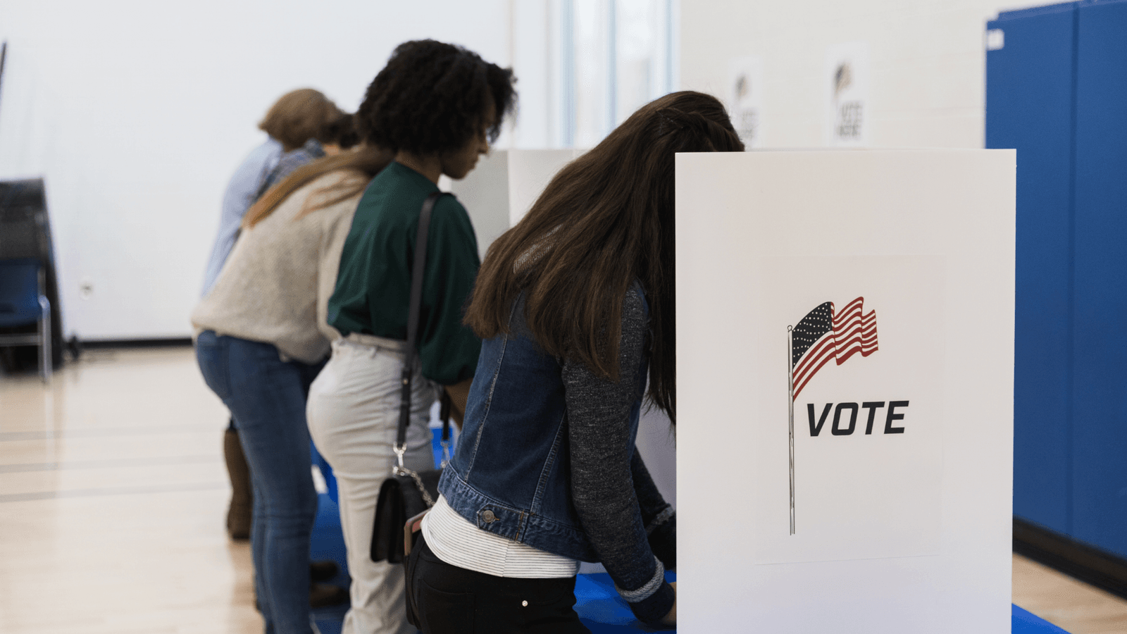 Voters casting their ballots at polling booths with a VOTE sign and an American flag.